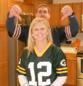 A tall man in a Chicago Bears jersey with thumbs down, behind a woman in a Green Bay Packers jersey.