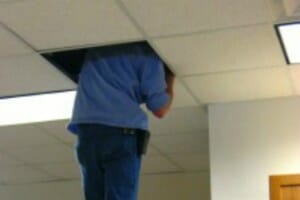 A maintenance man with his head and shoulders stuck above a ceiling panel.