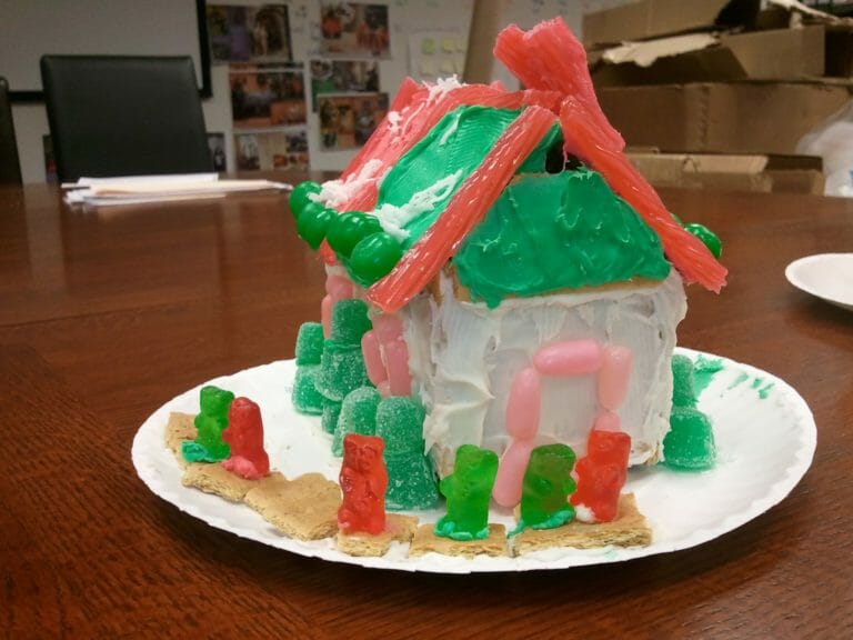 A gingerbread house decorated in red and green gummy candies, placed on an office table.