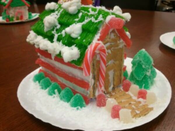A gingerbread house decorated in gum drops, a green roof, and a candy cane, placed on an office table.