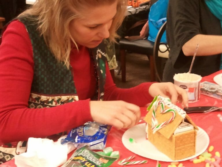 A woman decorating a gingerbread house with two candy canes in the shape of a heart.
