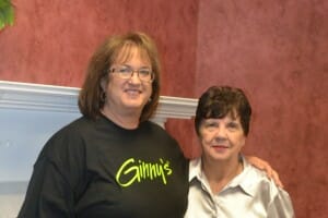 Ginny, a brunette woman with glasses and wearing a brown Ginny's T-shirt, with a brunette woman in a silver shirt.