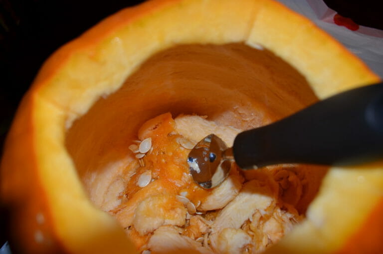 Close-up view of a kitchen scoop removing the seeds from inside a pumpkin.