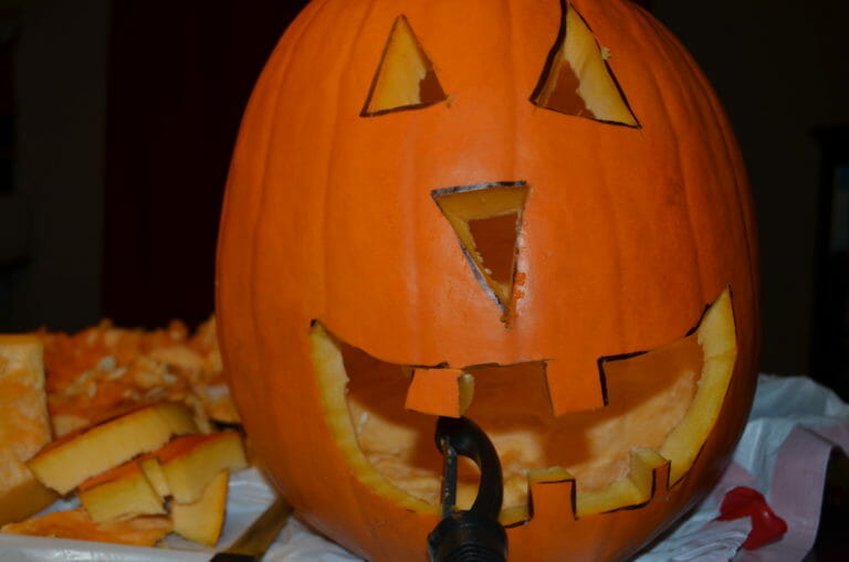 A Jack-o-Lantern face carved into an orange pumpkin, with a potato peeler smoothing the edges.
