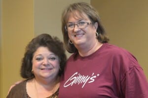 Ginny, a brunette woman wearing a brown Ginny's T-shirt, with Susie, a brunette woman in a brown cardigan.