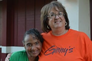 Ginny, a brunette woman wearing an orange Ginny's T-shirt, with Renee, a black woman in a green shirt.