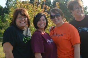 Four women wearing different colors of Ginny's T-shirts, including Ginny, herself.