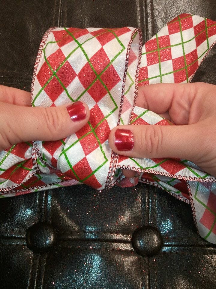 A woman's hands tying a red, green, and white plaid ribbon bow around a brown leather stool.