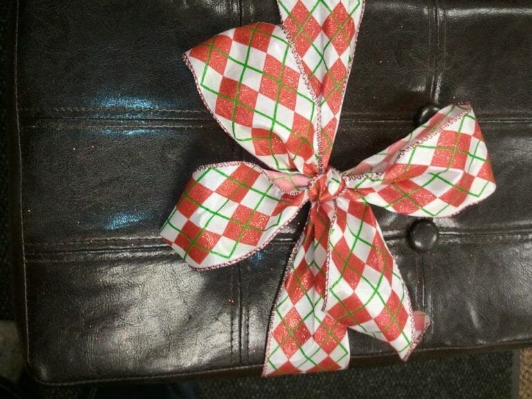 A red, green, and white plaid ribbon bow tied around a brown leather stool.