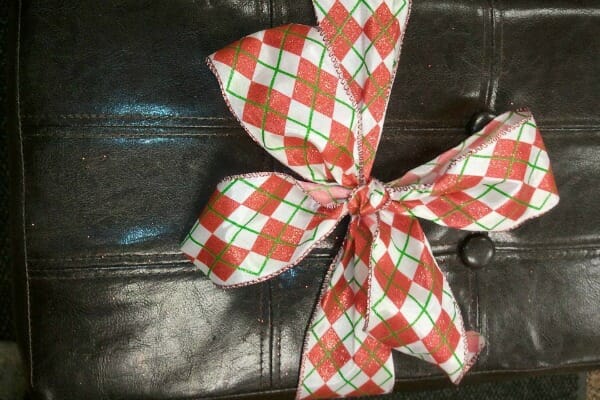 A red, green, and white plaid ribbon bow tied around a brown leather stool.
