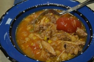 Close-up of an individual serving of Brunswick stew in a bright blue bowl, with a spoon.