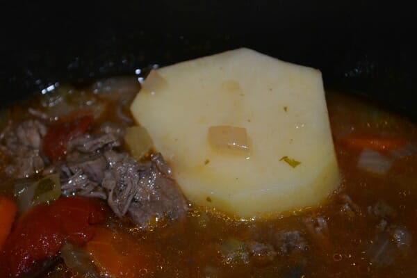 Close-up of a chunk of raw potato in a pot of Brunswick stew.