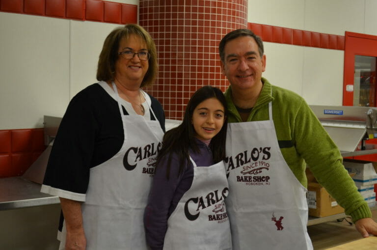 Ginny, a man and a girl in a bakery, wearing white Carlo's Bake Shop aprons.