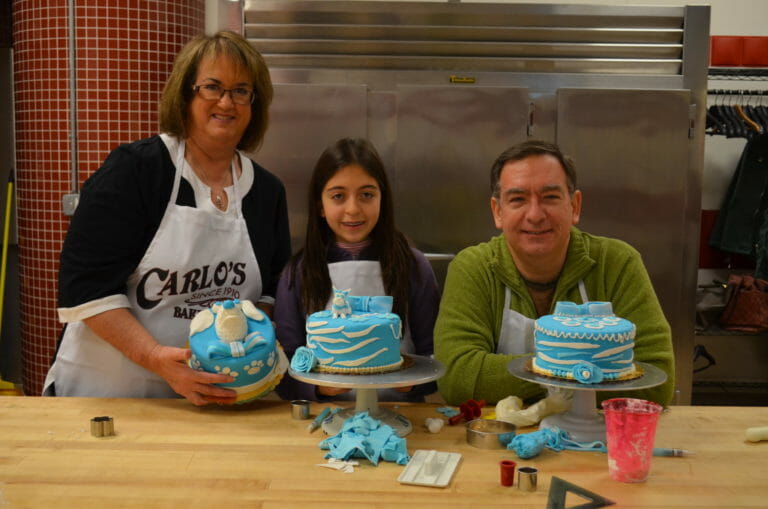 Ginny, a man, and a girl show off how they decorated their blue fondant layer cakes with white accents.