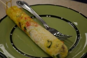 A rolled cooked omelette on a green plate with a fork.