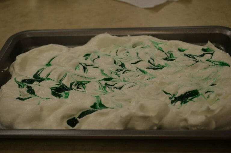 A baking pan filled with whipped topping, with green food color swirls cut in.