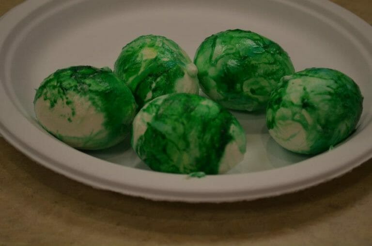 Six cooked eggs in the shell on a paper plate, covered with a mixture of green food coloring and whipped topping.