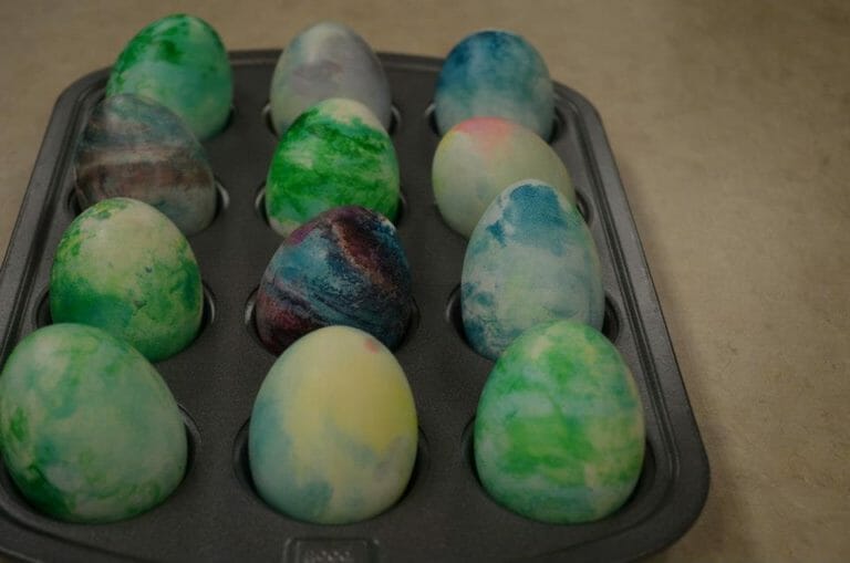 A dozen eggs swirled with different colors, placed in a muffin pan.