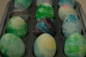 A dozen eggs swirled with different colors, placed in a muffin pan.