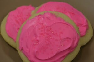 Three round sugar cookies topped with pink icing and red sugar crystals.