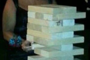 Close-up of a woman pulling a wood block from a stacked Jumbo Jenga game.