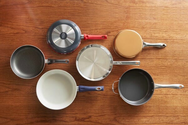 The tops and bottoms of six different fry pans, arranged on a wood table.