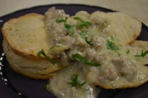 A purple plate filled with a serving of flaky biscuits and Country Sausage Gravy.