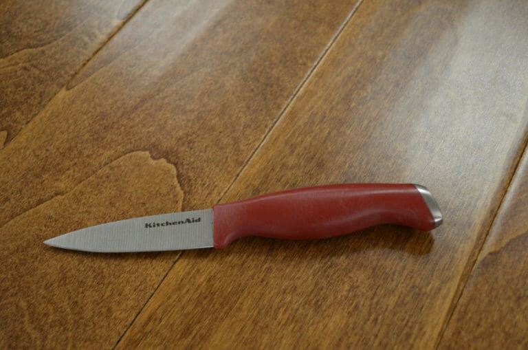 A KitchenAid Paring Knife with a red handle placed on a wood table.