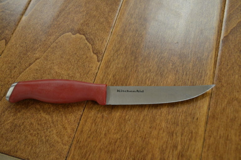 A KitchenAid Utility Knife with a red handle placed on a wood table.