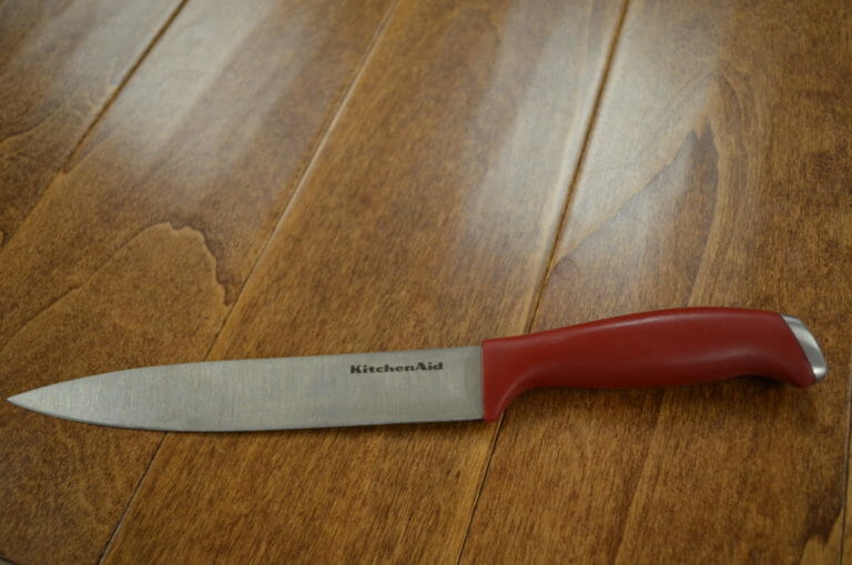 A KitchenAid Carving Knife with a red handle placed on a wood table.