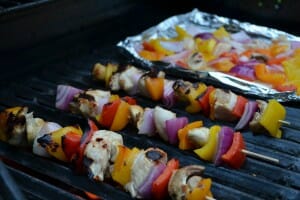 Three Chicken Shish Kabobs cooking on a flaming grill, with more pieces on foil.
