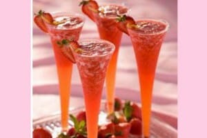 Four clear fluted glasses filled with Strawberry Punch, with fresh strawberry garnishes.