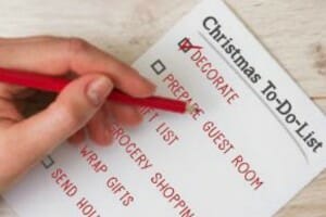 A person's hand checking boxes with a red pencil on a Christmas To-Do List.