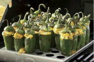 Several Jalapeno Poppers upright in a metal pan with holes, placed on a grill.