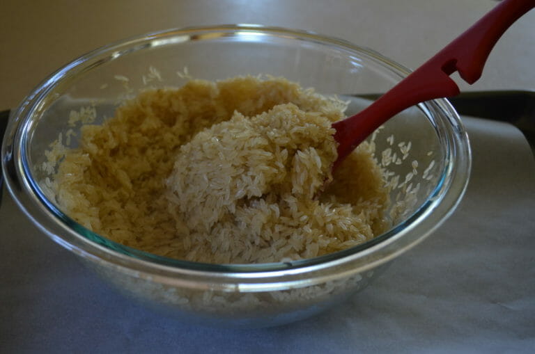 A red spoon in a clear mixing bowl filled with parboiled rice.