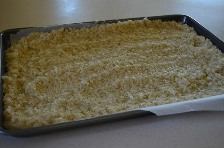 Parboiled rice spread out on a jelly roll pan lined with parchment paper.