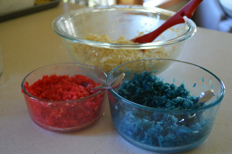 Three clear bowls of parboiled rice, one white, one colored red, and one colored blue.