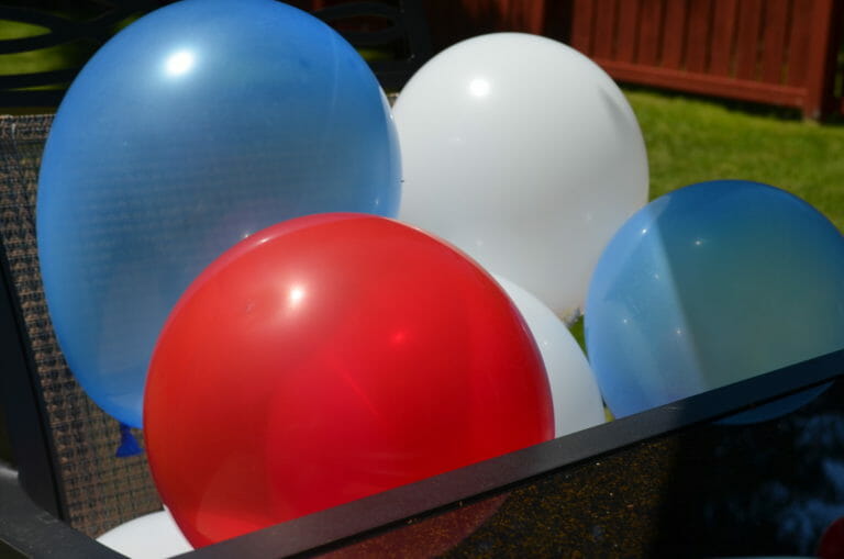 Red, white, and blue balloons corralled in a chair outside.