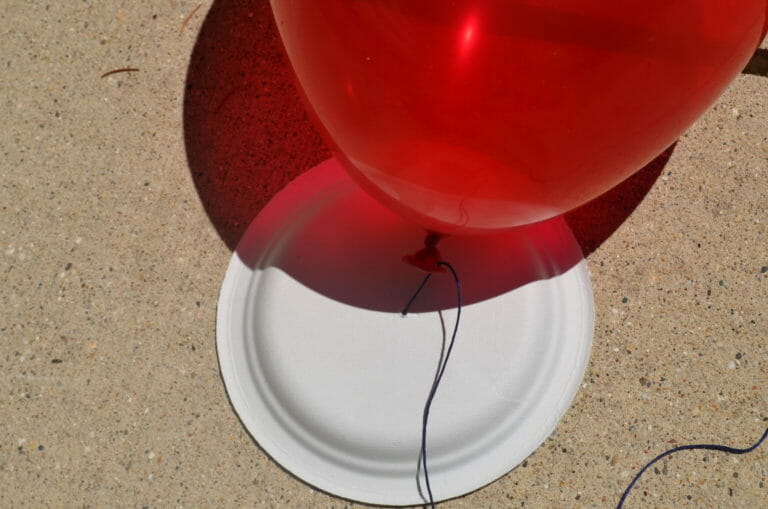 A red blown up balloon strung on blue embroidery floss through a hole poked on the tied end.