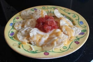 A serving of Nachos on a colorful plate, with two kinds of melted cheese and red salsa in the center.