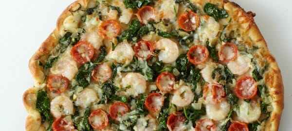 A homemade Shrimp Pizza with cherry tomatoes, spinach, shrimp and cheese.