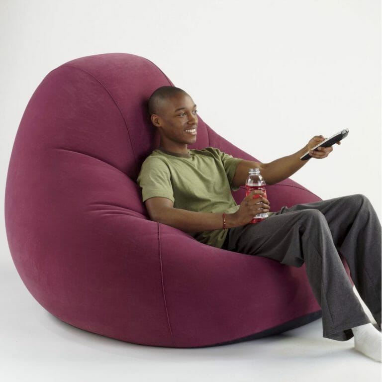 An African-American man lounging with a beverage and a remote control in a large burgundy bean bag chair.