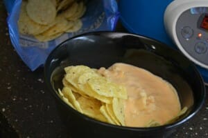 A black bowl with corn chips and Buffalo Chicken Dip, next to a blue bag of chips.