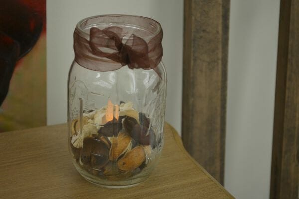 A Mason jar with potpourri and a lit tea light inside, and tied with a sheer brown bow.