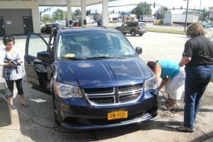 Three women by a van at a gas station, with one putting air into a tire.