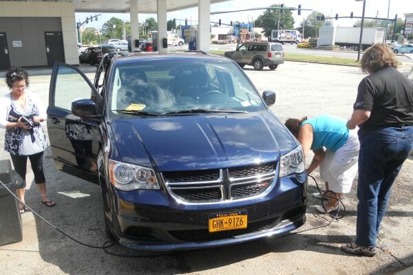 Three women by a van at a gas station, with one putting air into a tire.