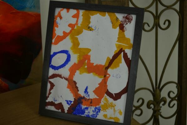 Framed artwork with different kinds of leaves painted over with paints, then removed, to show their shapes.