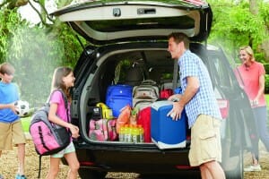 A mother, father, a boy and a girl packing the back of a van with drinks, a cooler and backpacks, ready for a road trip.
