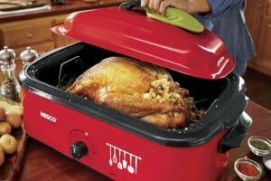 A large red Nesco brand electric roaster/slow cooker, filled with a whole turkey and bread stuffing.