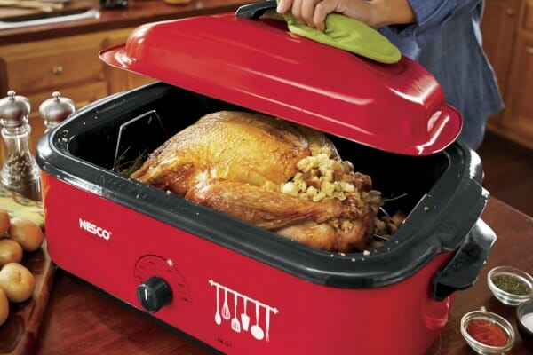 A large red Nesco brand electric roaster/slow cooker, filled with a whole turkey and bread stuffing.